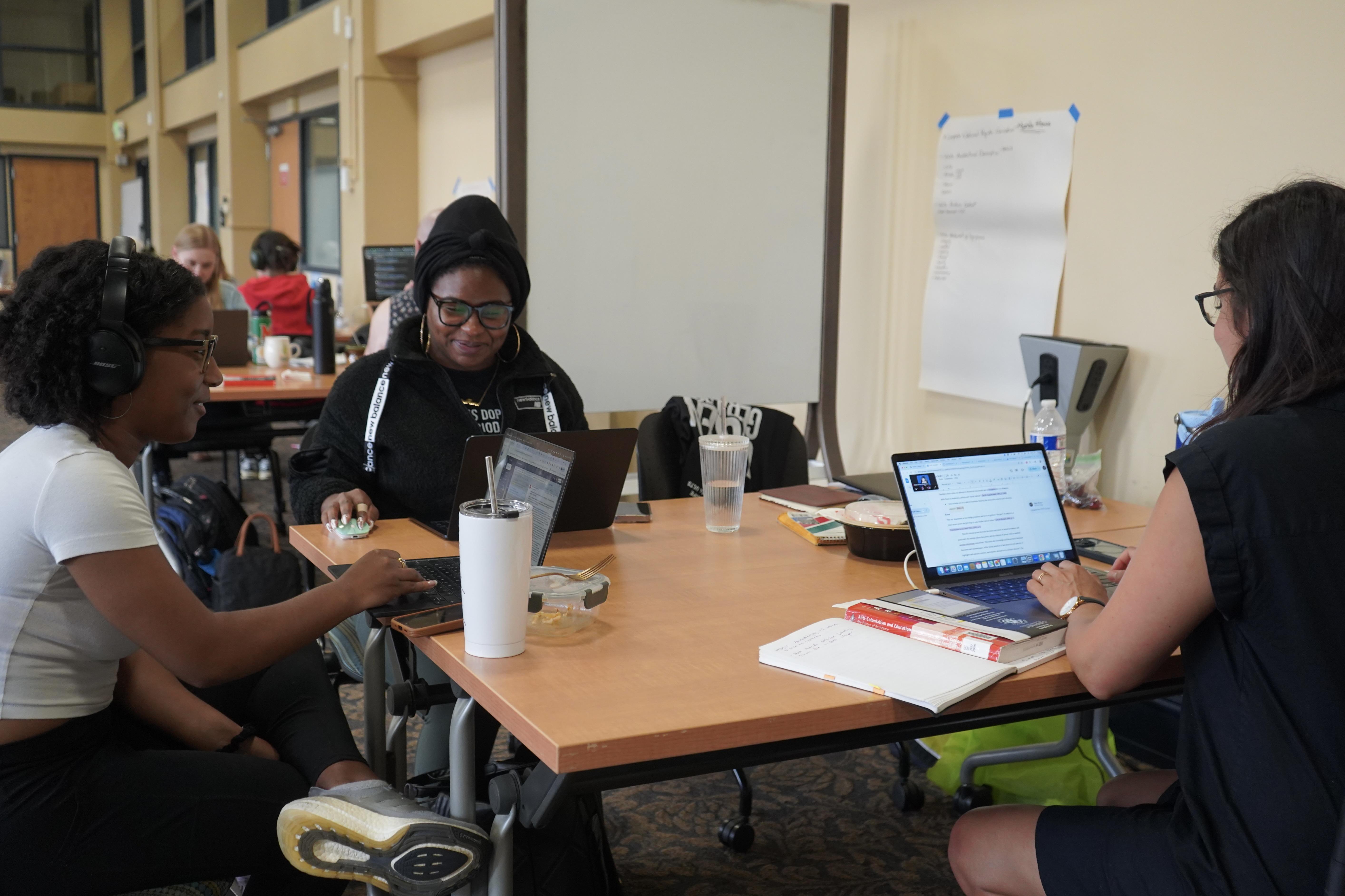 Graduate students smiling and typing on laptops at Writing Retreat